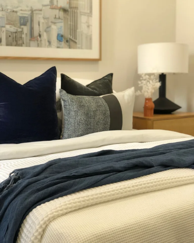 Layered bedding with textured pillows, a waffle throw, and a dark blue linen layer