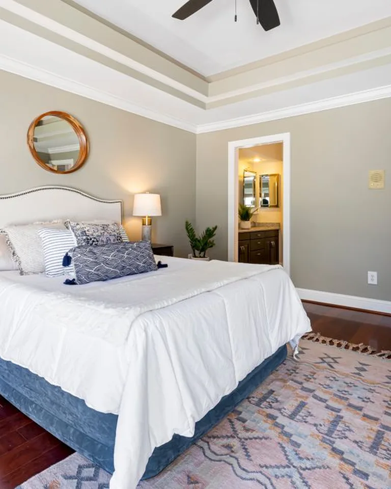 Patterned area rug extending beside a dressed bed on a dark wood floor