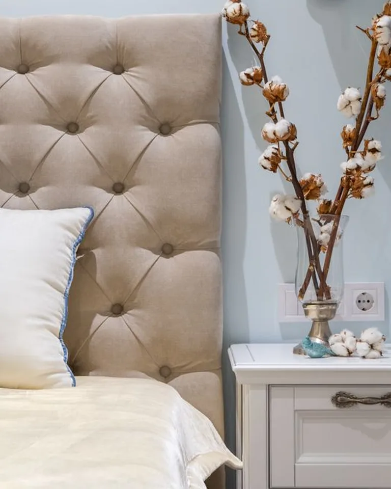 Tufted beige upholstered headboard with blue and white pillows and a white nightstand