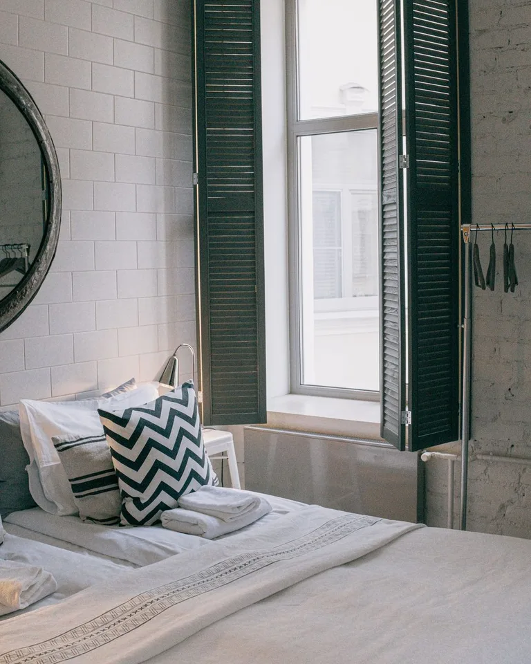 Bed styled with patterned chevron and striped throw pillows against a white brick wall