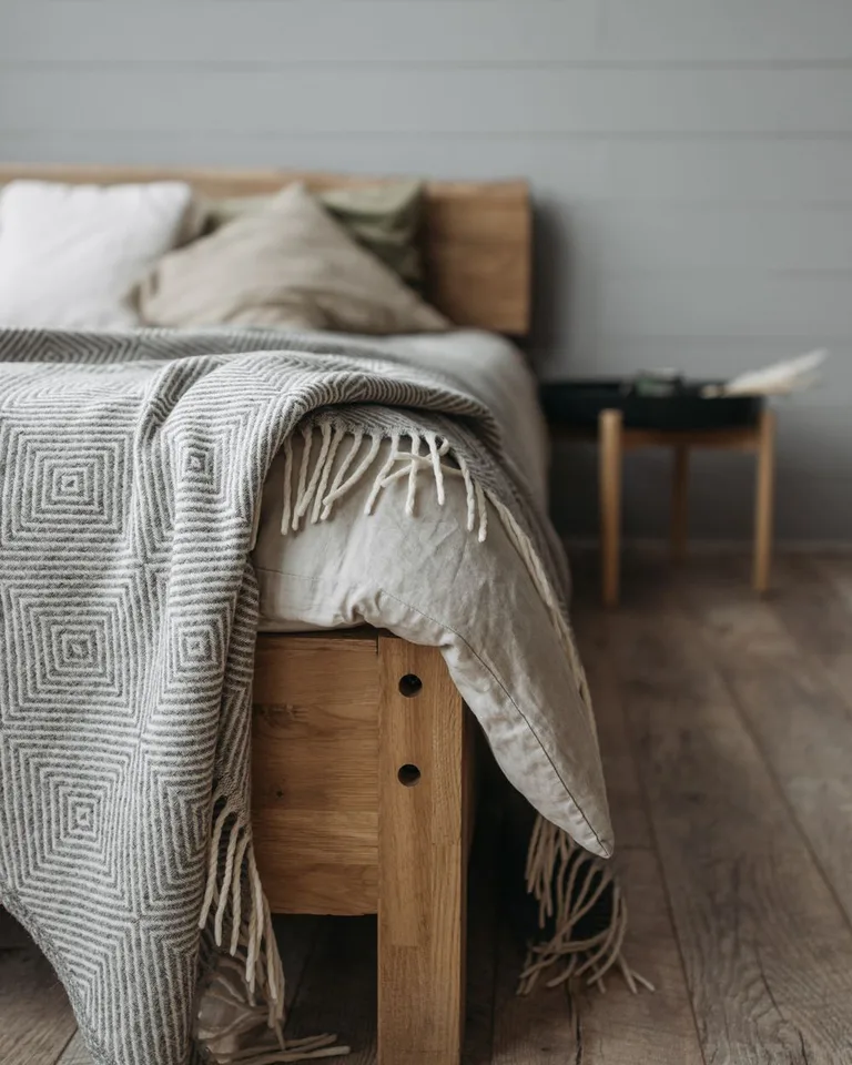 Patterned woven throw with fringe draped across the foot of a wooden bed