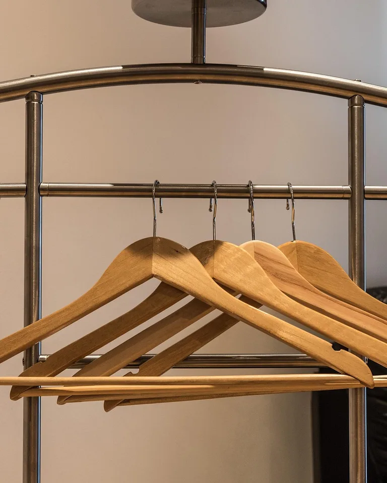 Open clothing rail with wooden hangers holding shirts and jackets in a bedroom
