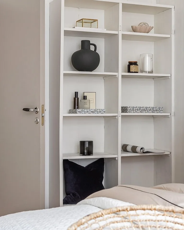 Tall narrow white shelving unit standing beside a bed in a small bedroom