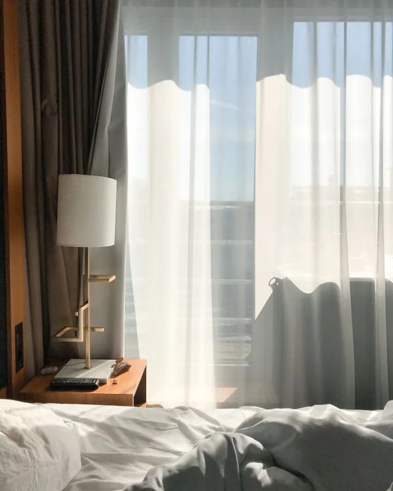 Sheer white curtains on a wide curtain rod softening a bedroom window wall