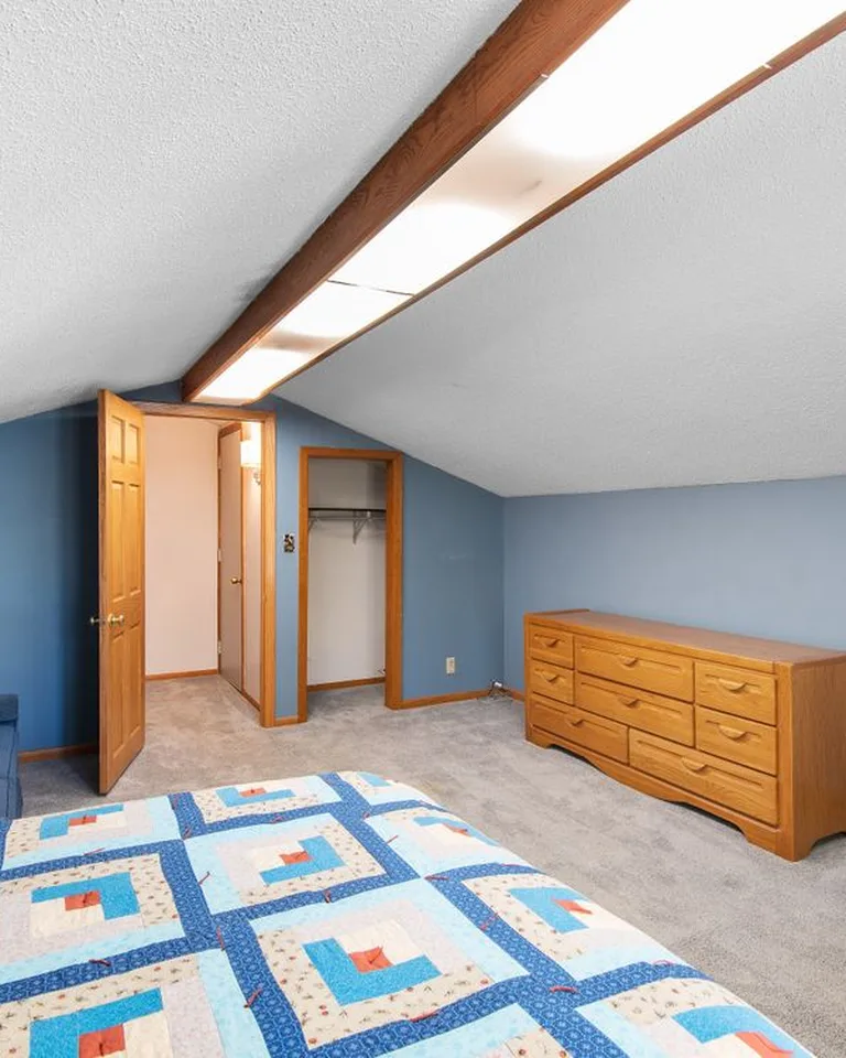Bedroom with a sloped ceiling, a patterned quilt, and a wooden dresser