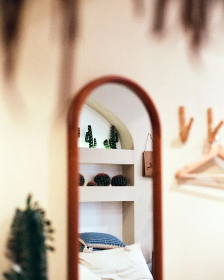 Arched wooden-framed mirror reflecting a bedroom bed and shelves