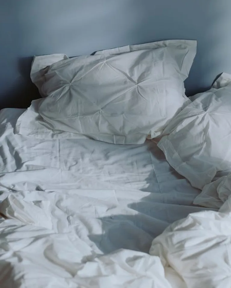 Bed dressed in rumpled white bedding in soft daylight