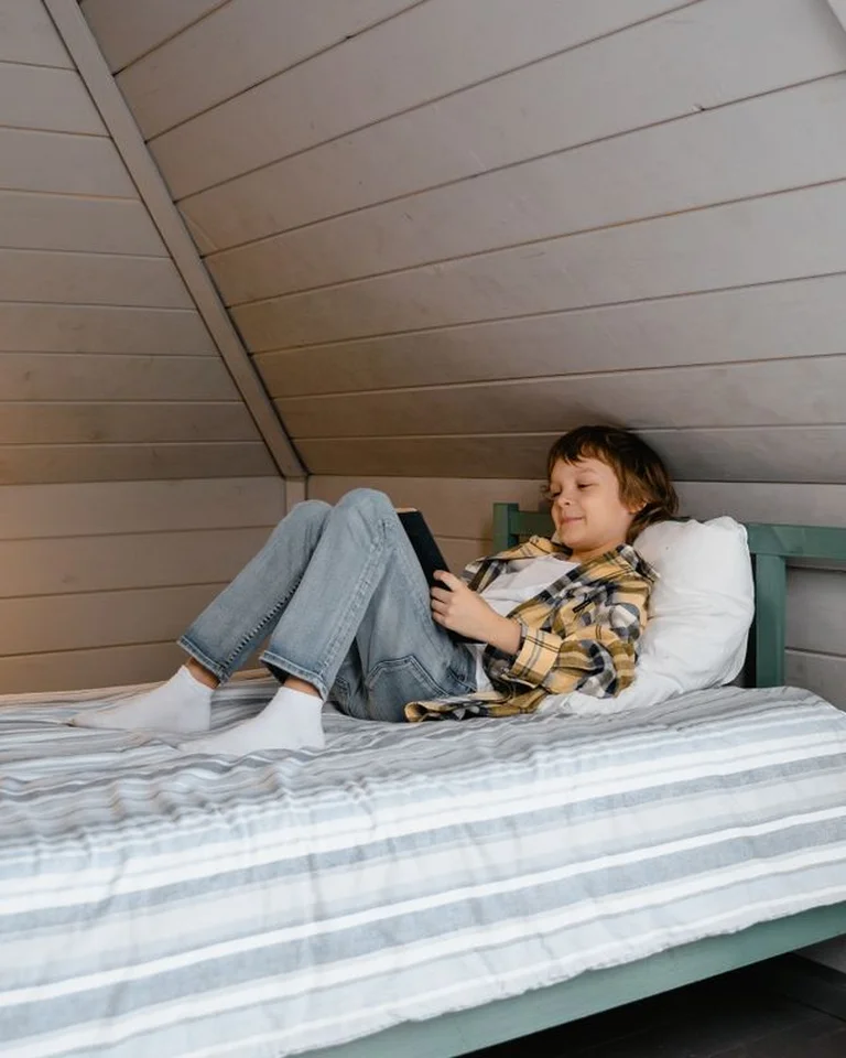 A person relaxing on a bed in an attic bedroom with a sloped ceiling