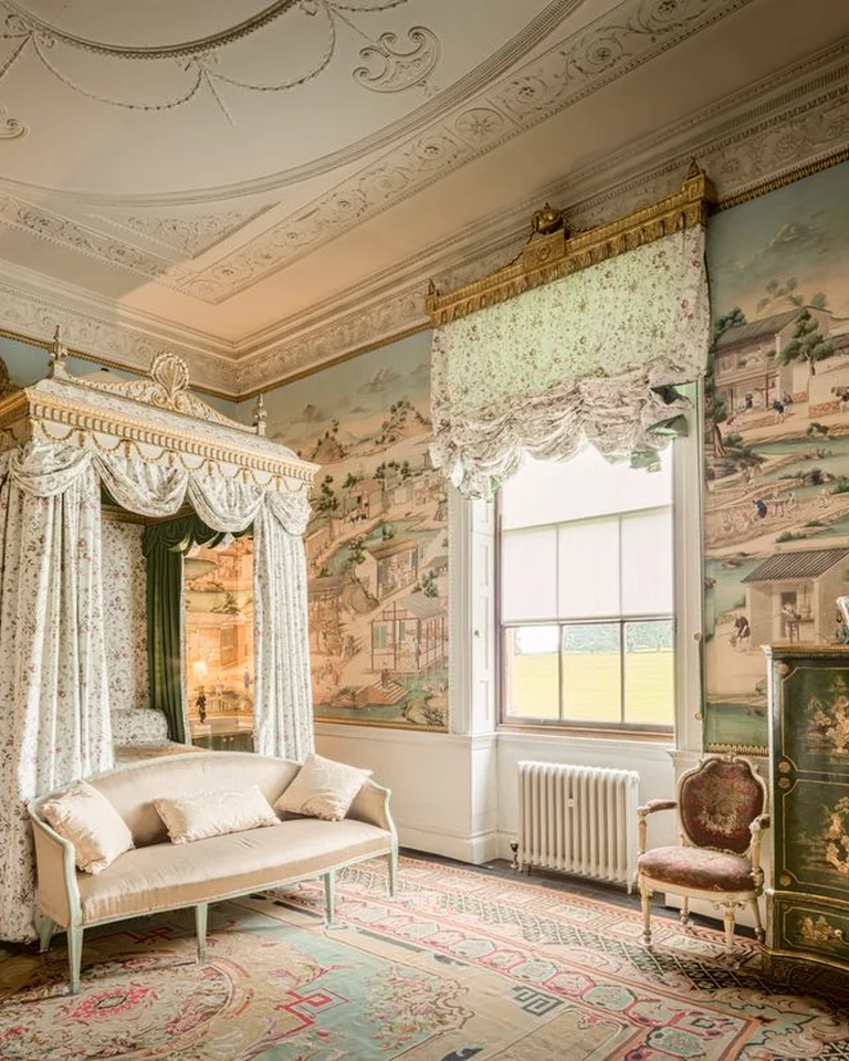 An elegant bedroom with tall windows, patterned wallpaper, and a sitting area in a separate zone