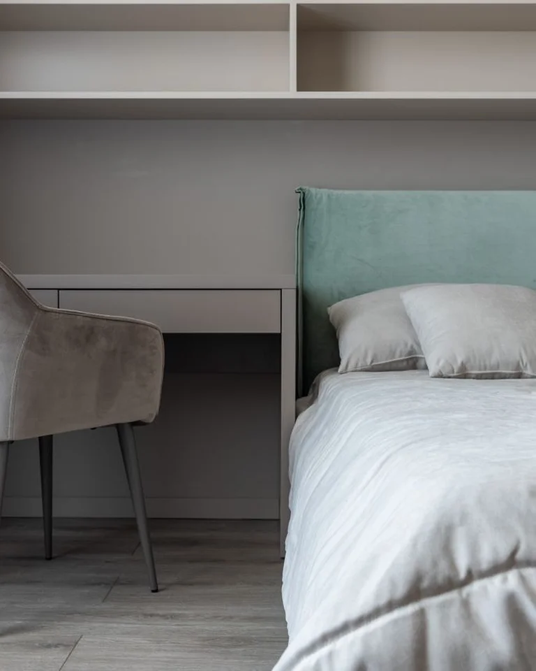 A bedroom workspace with a desk, chair, and shelving beside the bed