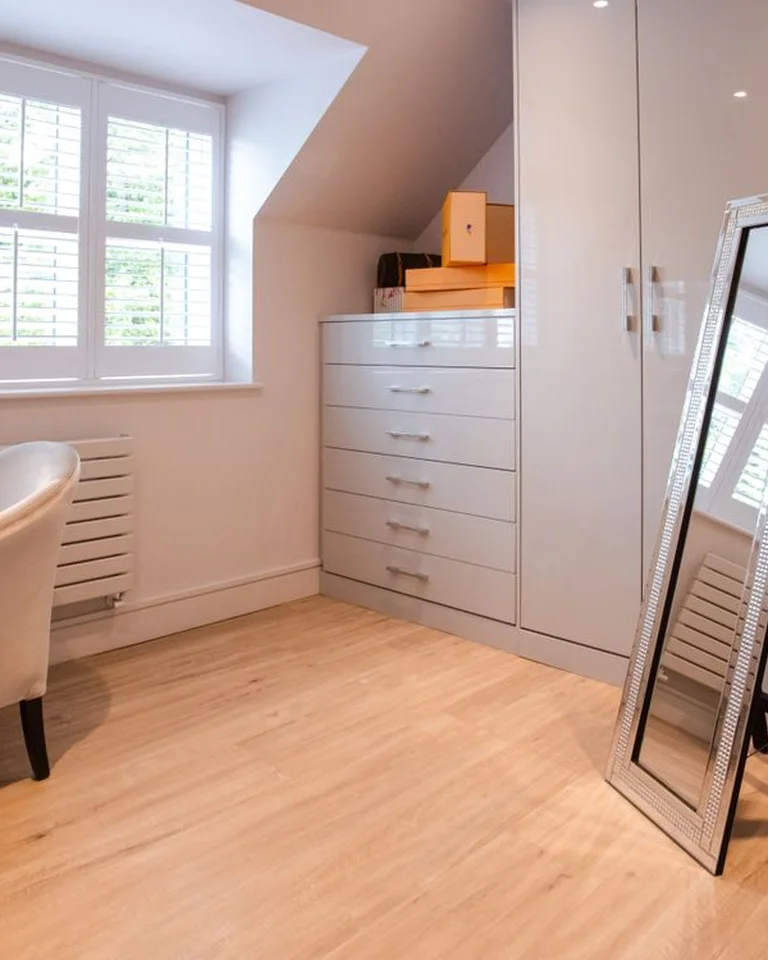 A bright bedroom with a full-length leaning mirror beside a white wardrobe and drawers