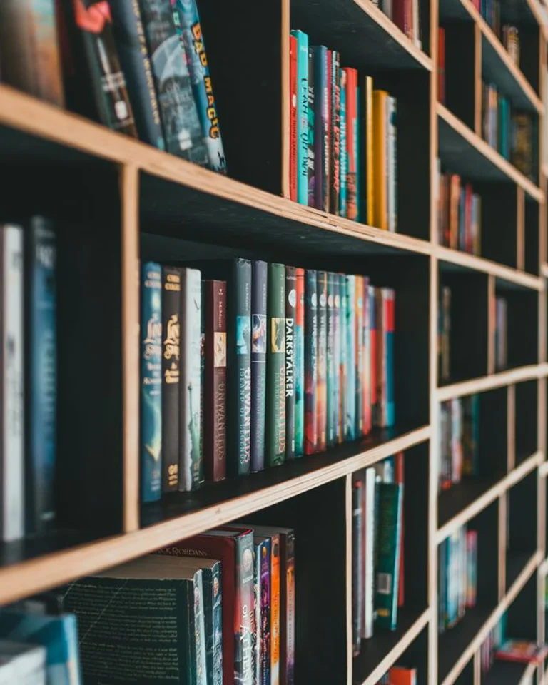 A tall bookshelf wall filled with books beside a bedroom seating area