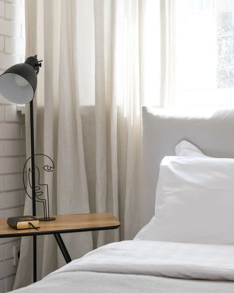 A minimal, bright bedroom with white bedding, sheer curtains, and a clear open floor