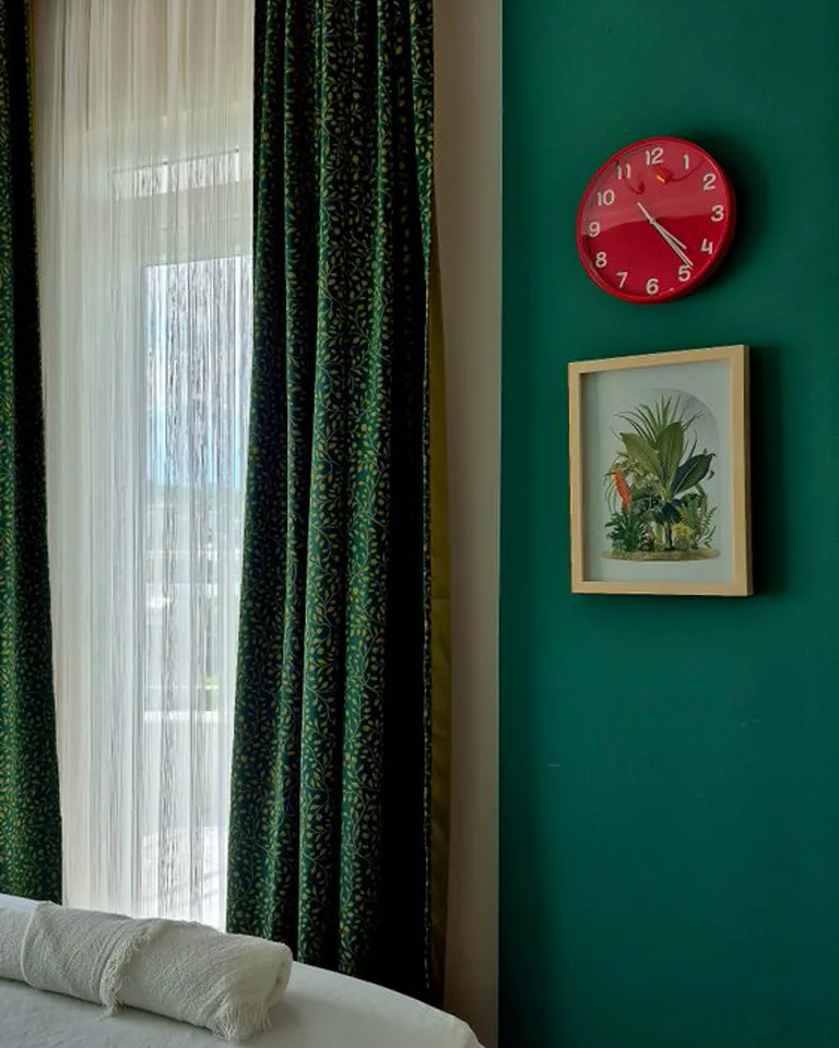 Bedroom wall painted deep green with curtains and framed art