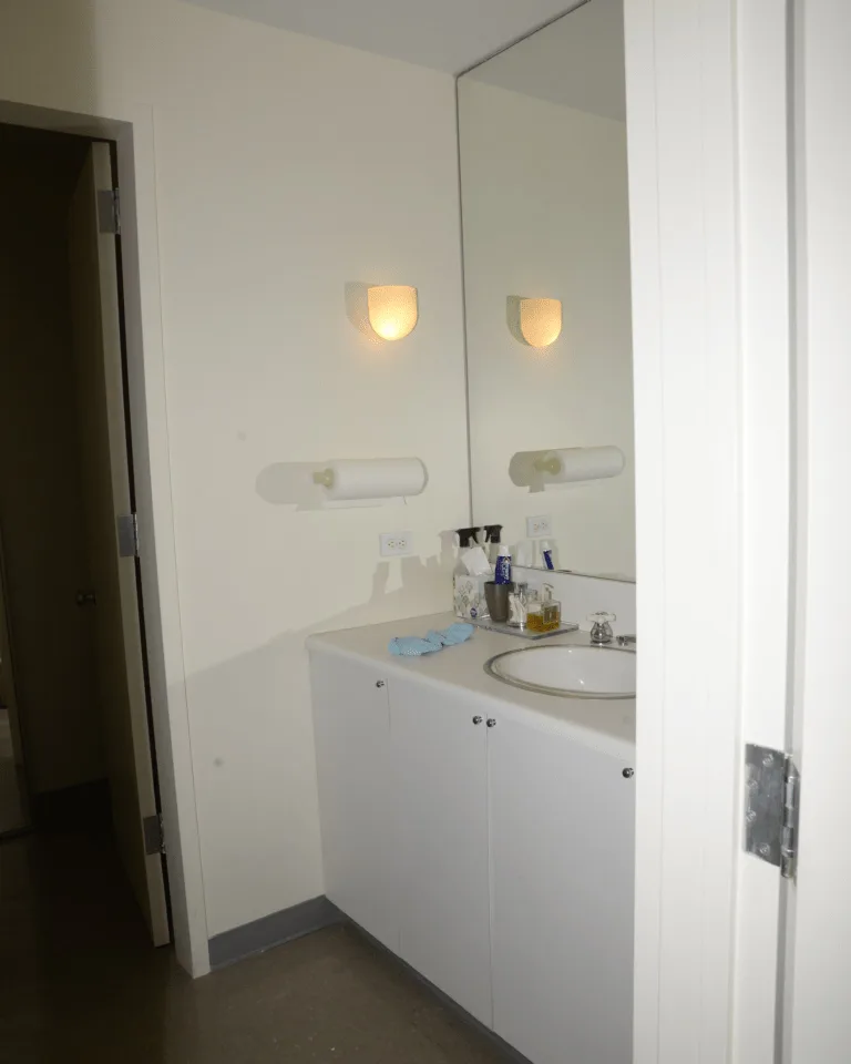White bathroom vanity with mirror illuminated by wall sconces