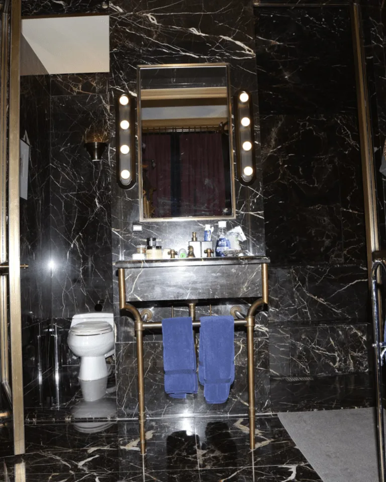 Bathroom mirror surrounded by round vanity bulbs in a dark marble bathroom
