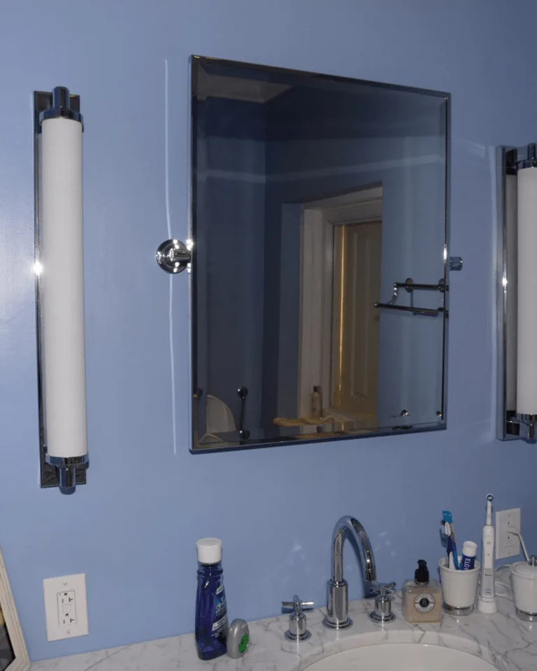 Bathroom mirror with vertical light bars mounted on a blue wall