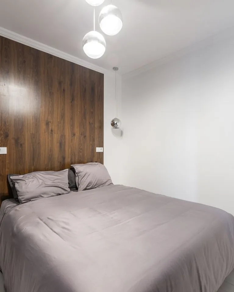 Small bedroom with light walls and a warm wood accent wall behind the bed