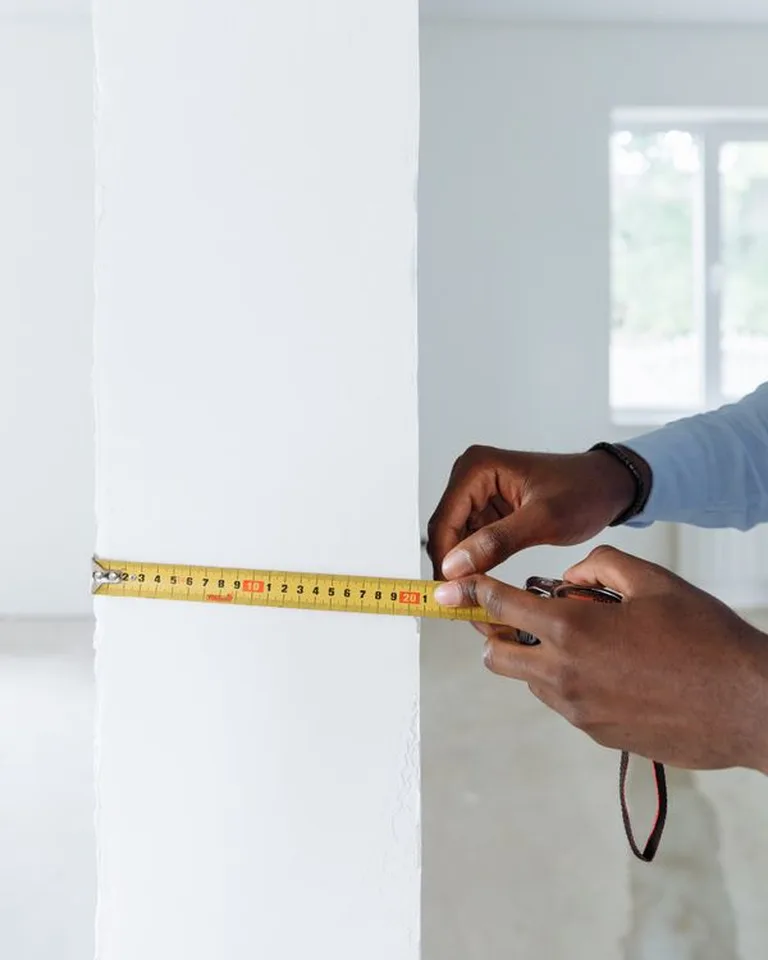 Person measuring a bedroom floor with a tape measure while planning furniture layout