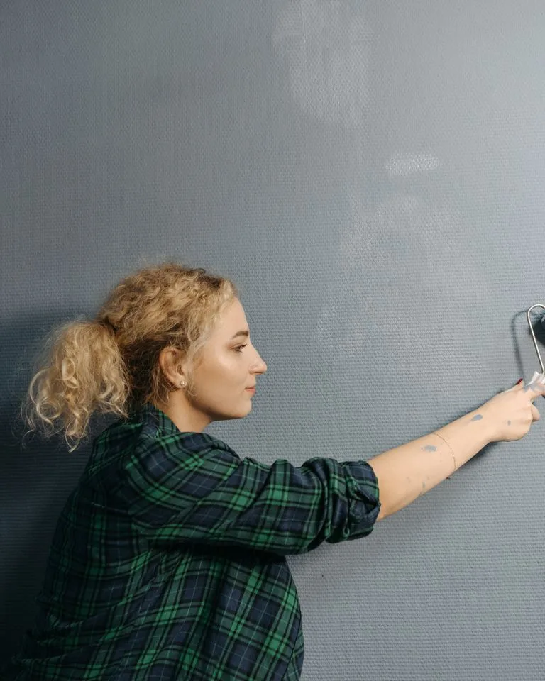 Person painting a bedroom wall with a roller during a DIY makeover