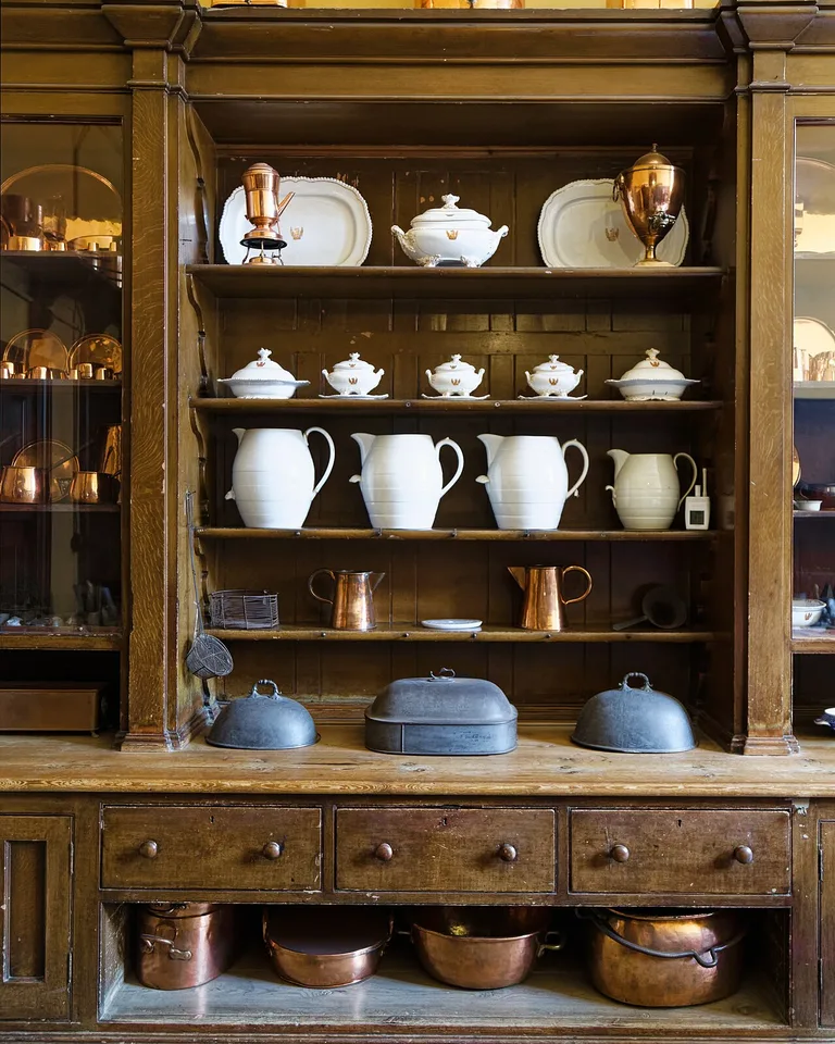 Antique wooden kitchen cupboard styled with copper pots and white ceramics