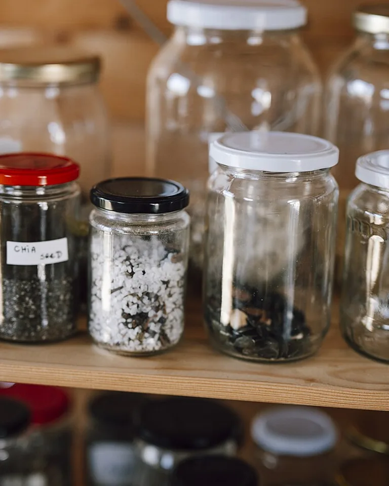 Glass pantry storage jars lined up on a wooden shelf