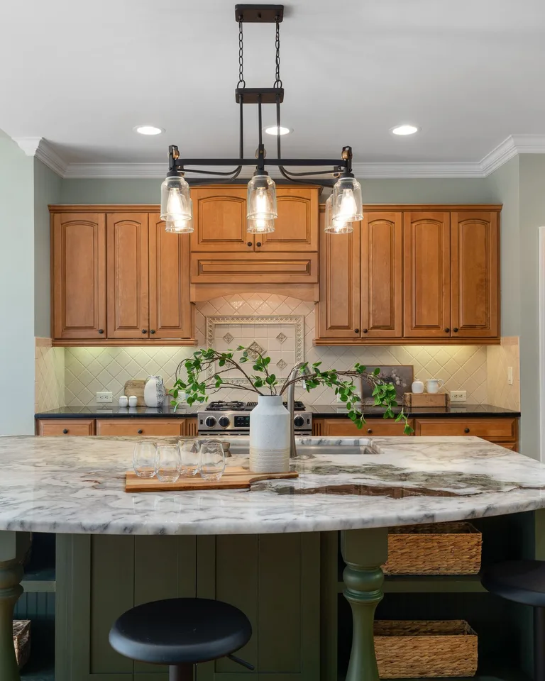 Dark green kitchen island with a marble countertop and glass pendant lights