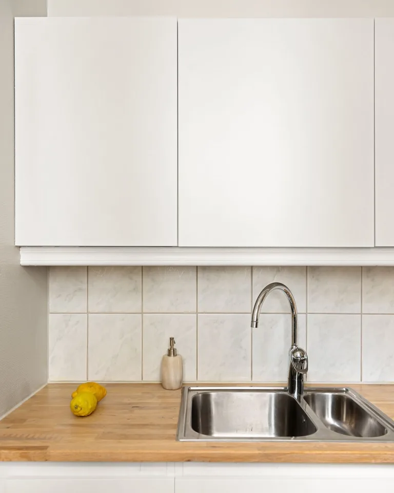 White kitchen cabinets with a marble tile backsplash and chrome faucet