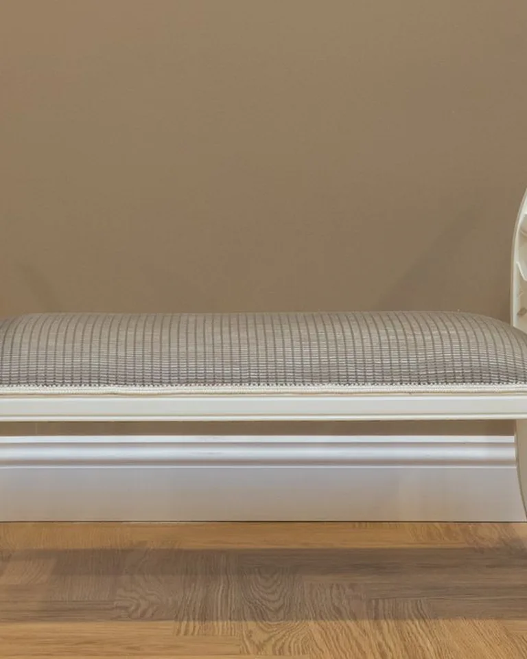 White bench with a gray upholstered cushion seat against a wall