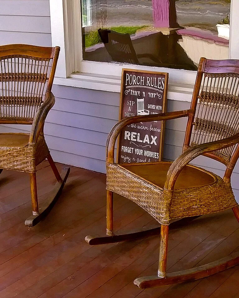 Two wicker rocking chairs on a front porch with a porch rules sign