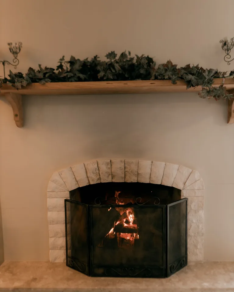 Wooden fireplace mantel styled with a greenery garland above a lit fire