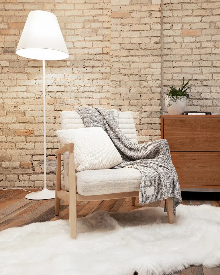 Gray knit throw draped over a cream armchair beside a floor lamp
