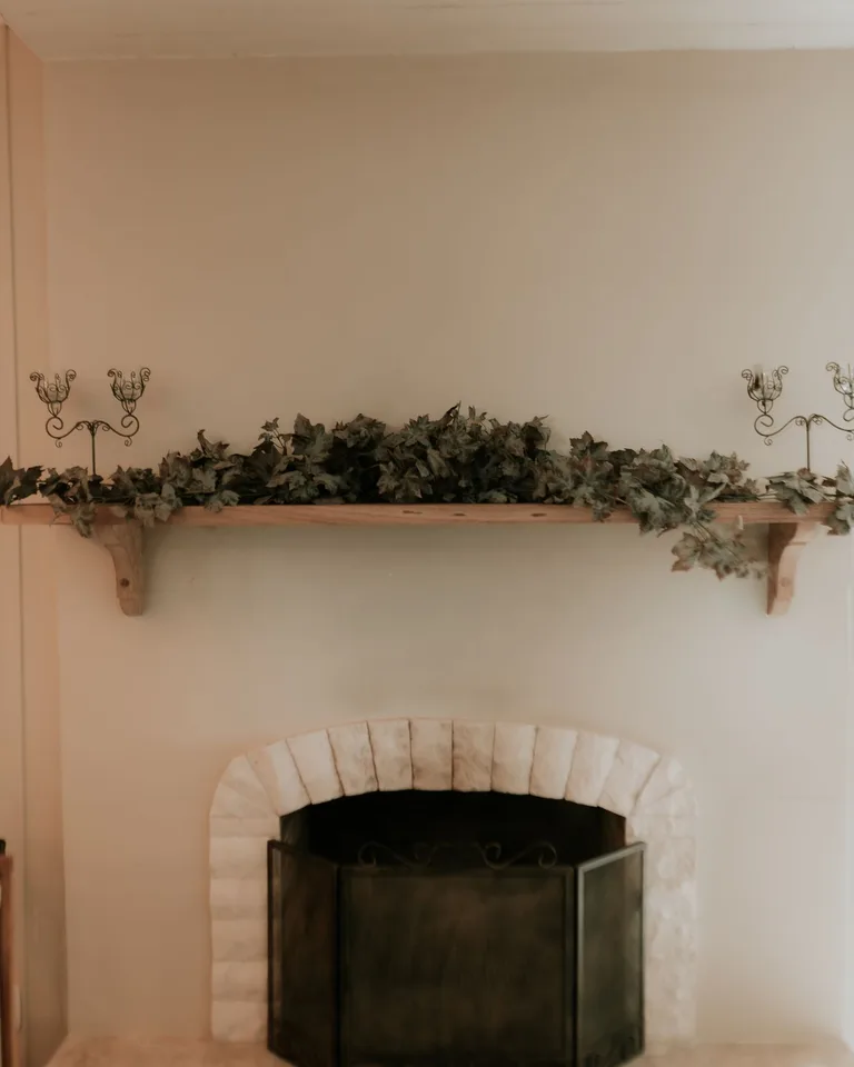 Fireplace mantel with a dried greenery garland and iron candle sconces