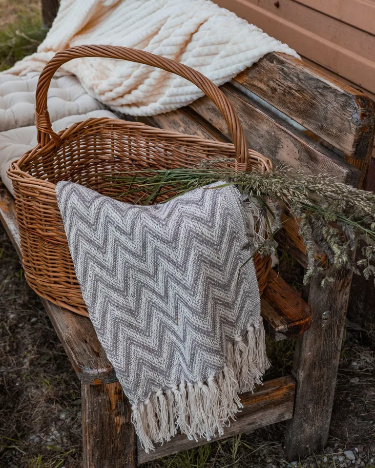 Wicker basket holding folded blankets on a rustic bench
