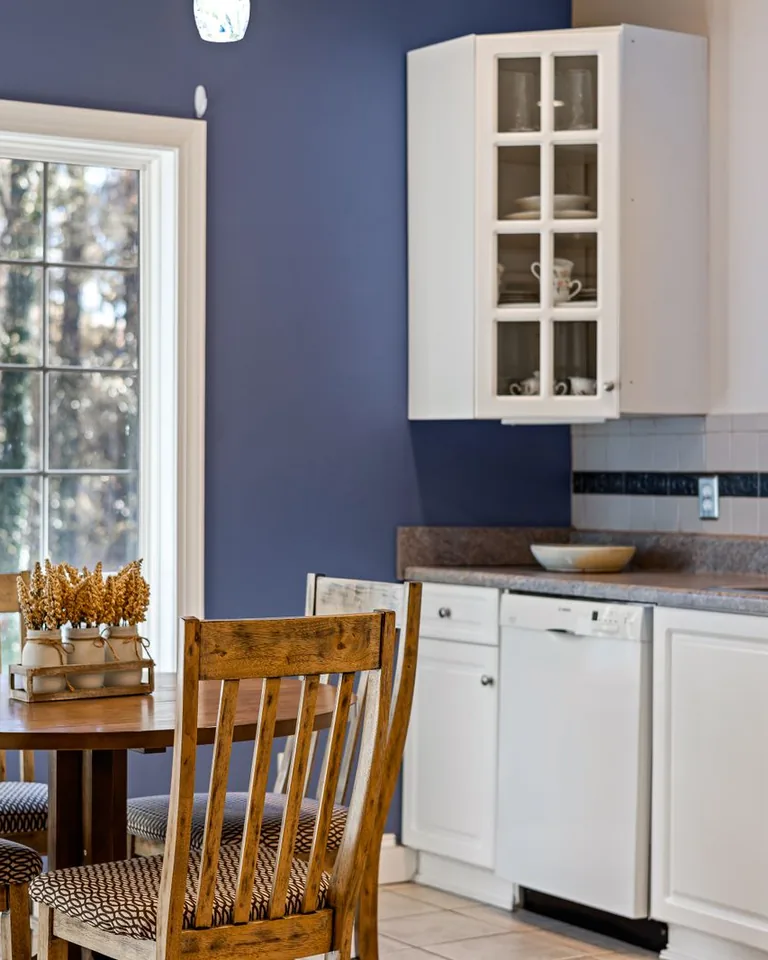 Bright kitchen with a round wooden dining table, white cabinets and large windows