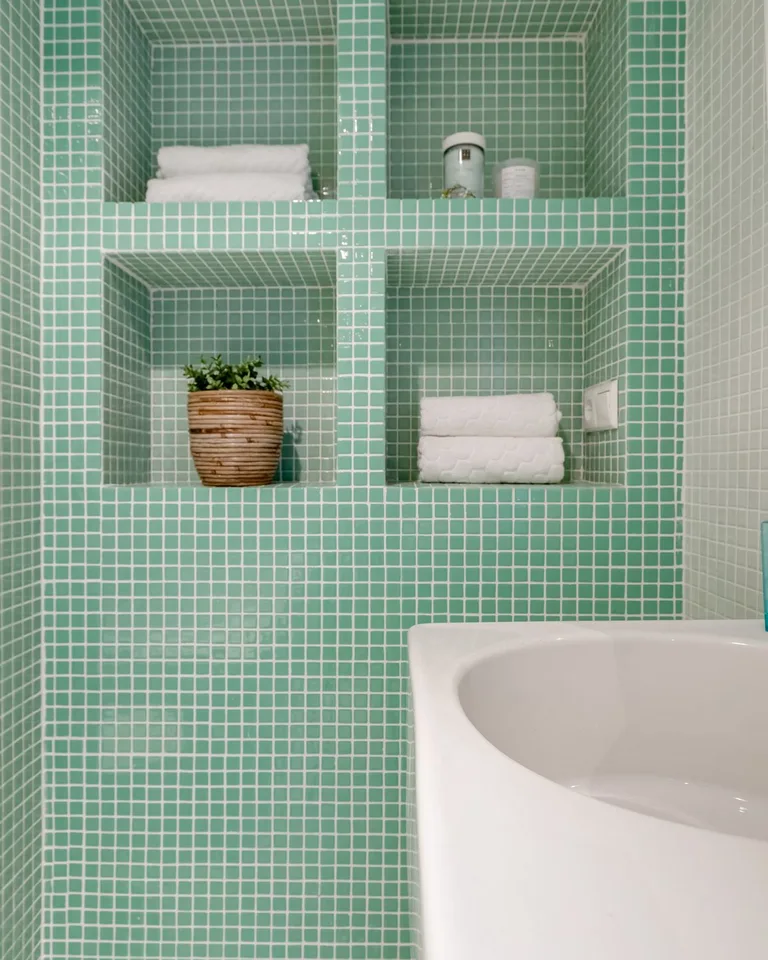 Green mosaic tile walls in a moody small bathroom with white fixtures