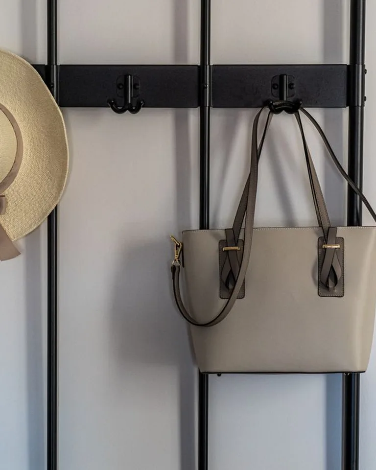 A black wall-mounted rack holding a straw hat and a handbag
