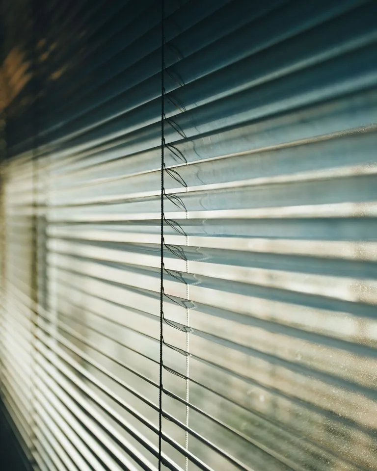 Sunlight filtering through natural slatted window blinds in a bedroom