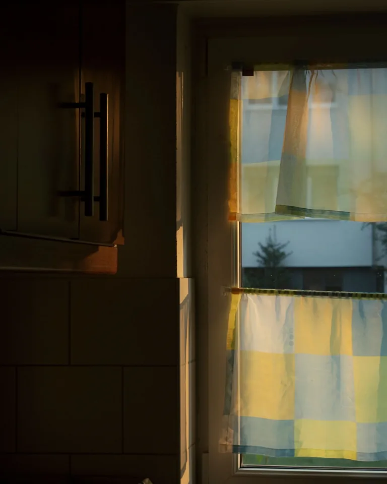 Kitchen window with checkered cafe curtains in warm sunset light