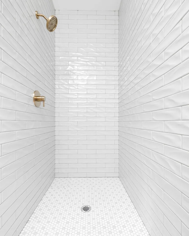 Minimalist white subway tile shower wall with brass fixtures