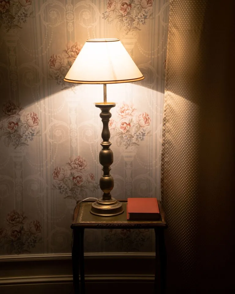 Aged brass table lamp glowing on a nightstand in a beige bedroom
