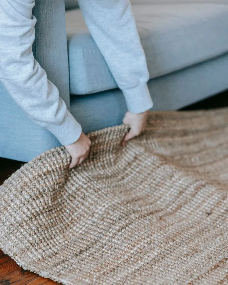 Hands laying a natural jute area rug on a wood floor