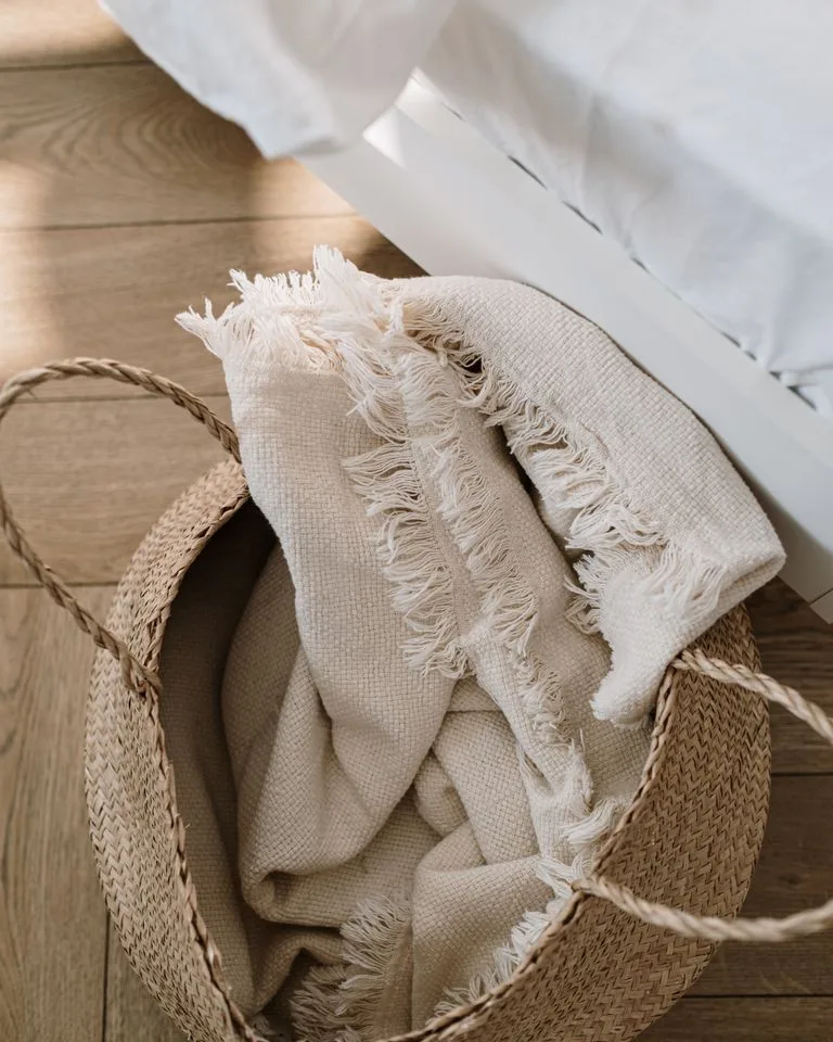 Woven seagrass basket holding folded blankets in a bedroom corner