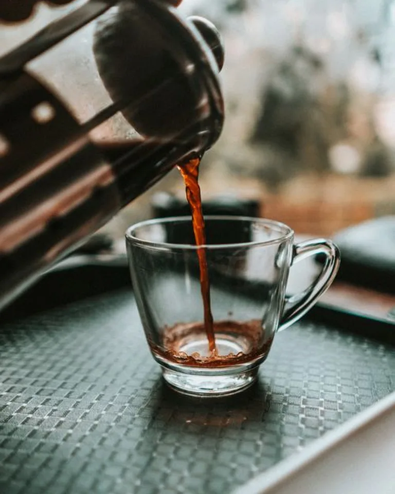 Hand pouring fresh coffee from a moka pot into a ceramic mug