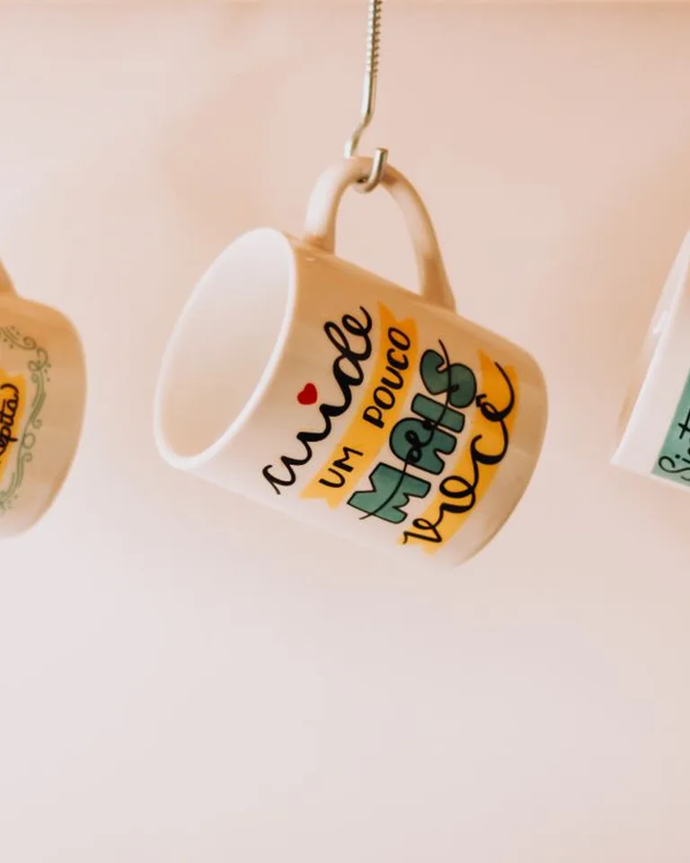 Coffee mugs hanging from hooks under a kitchen shelf