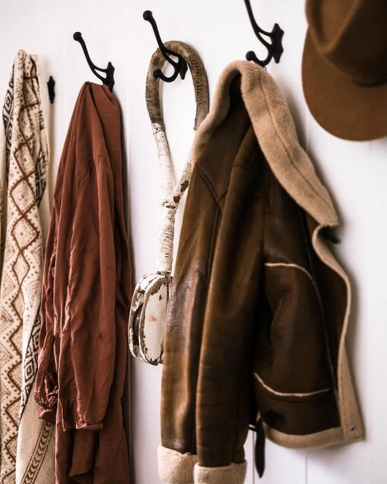A wooden wall rail with hooks in a bedroom holding bags and a jacket