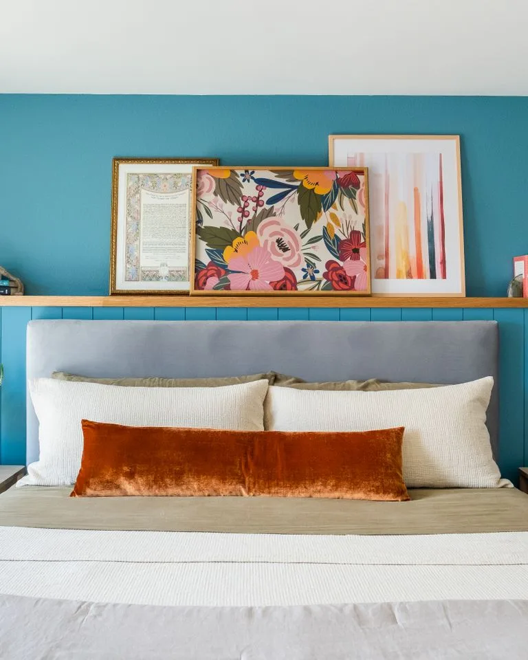 Picture ledge with layered framed art above a bed headboard