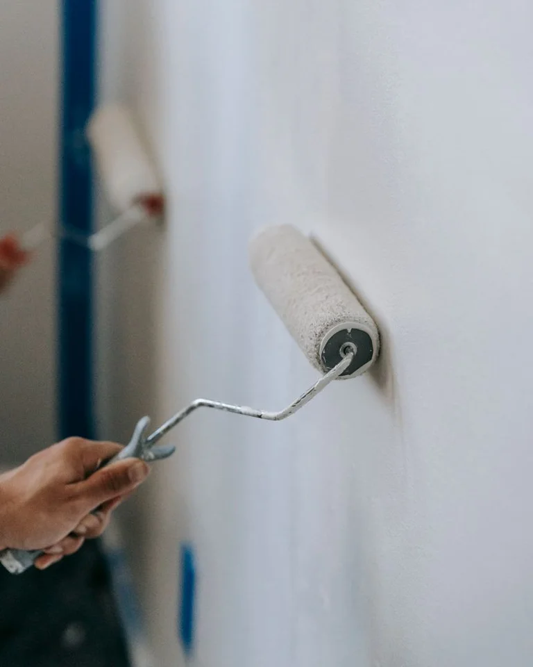 A paint roller applying fresh paint to a wall with blue painter's tape along the trim
