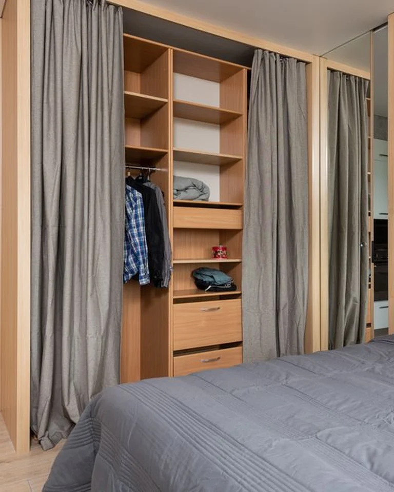 An organized open closet with curtains in a narrow bedroom