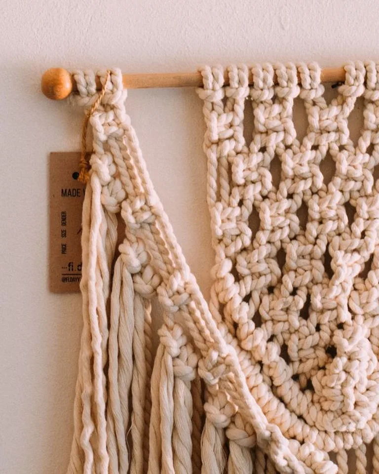 A cream macramé wall hanging with fringe above a bed in a no-closet bedroom